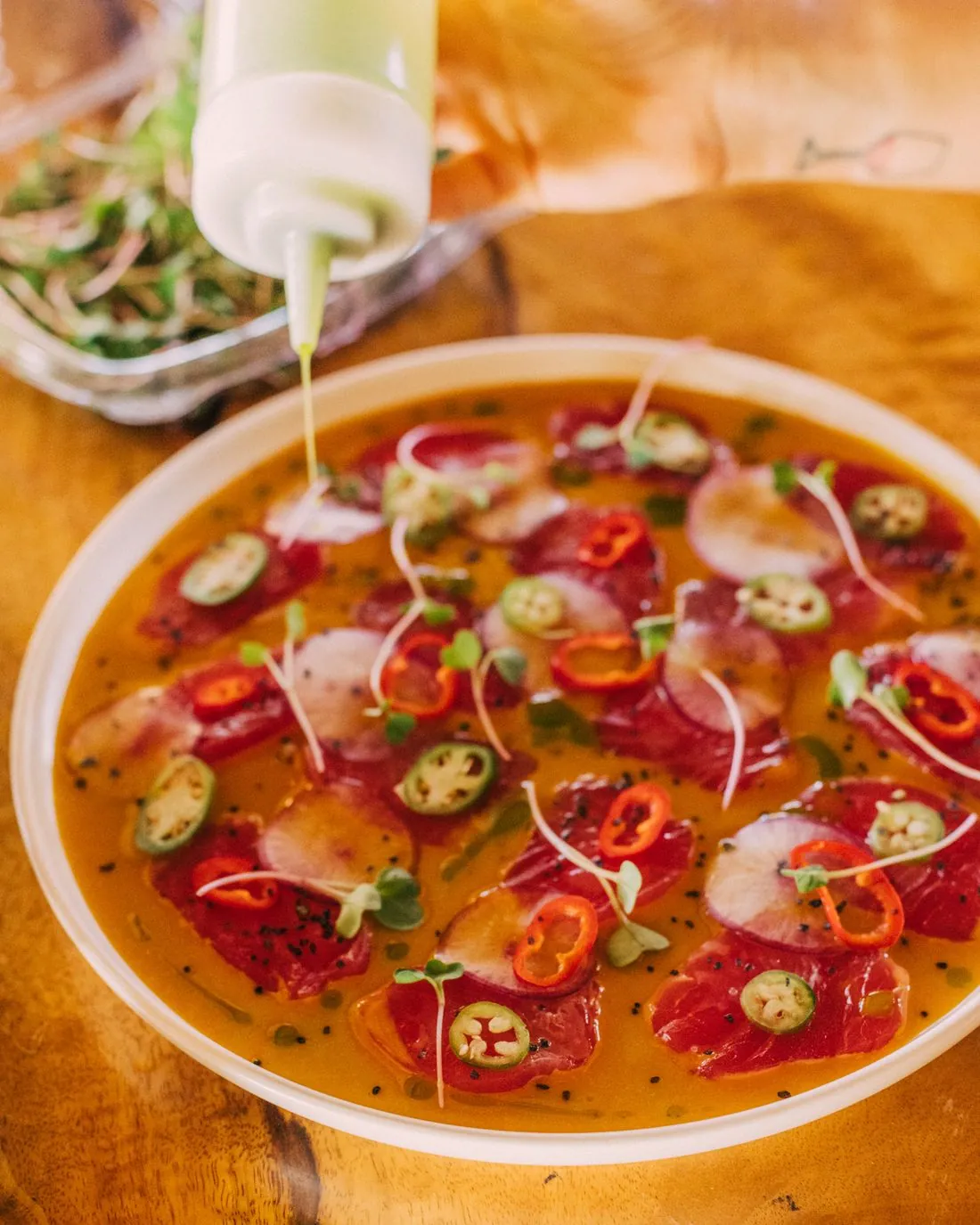 Green herb oil being squeezed over tuna crudo with chiles and radish